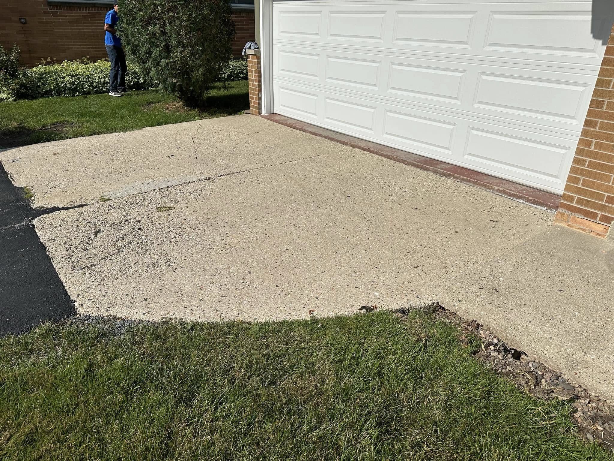 Existing deteriorated concrete apron at garage base with surface crumbling and wear at lawn edge